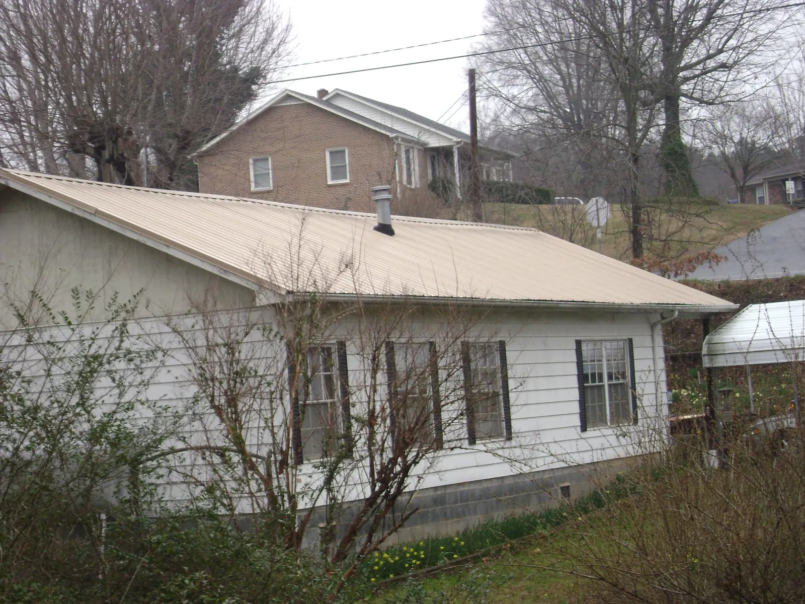 Tan metal roof on a white sided house set into a hillside — Commercial Roofing by Roofing Brothers in Centralia